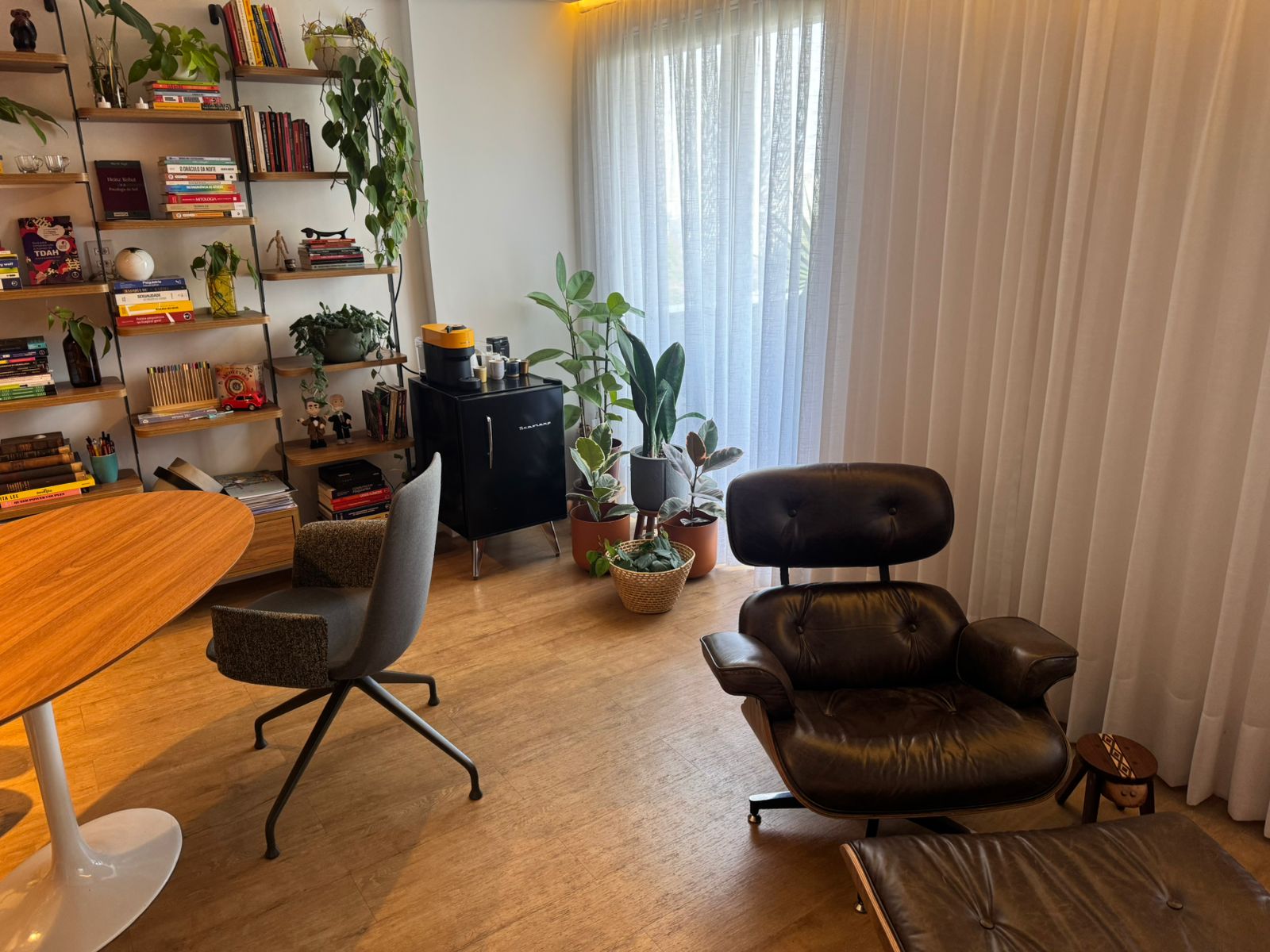 Consultório amplo com poltrona Eames, mesa oval e estantes com livros