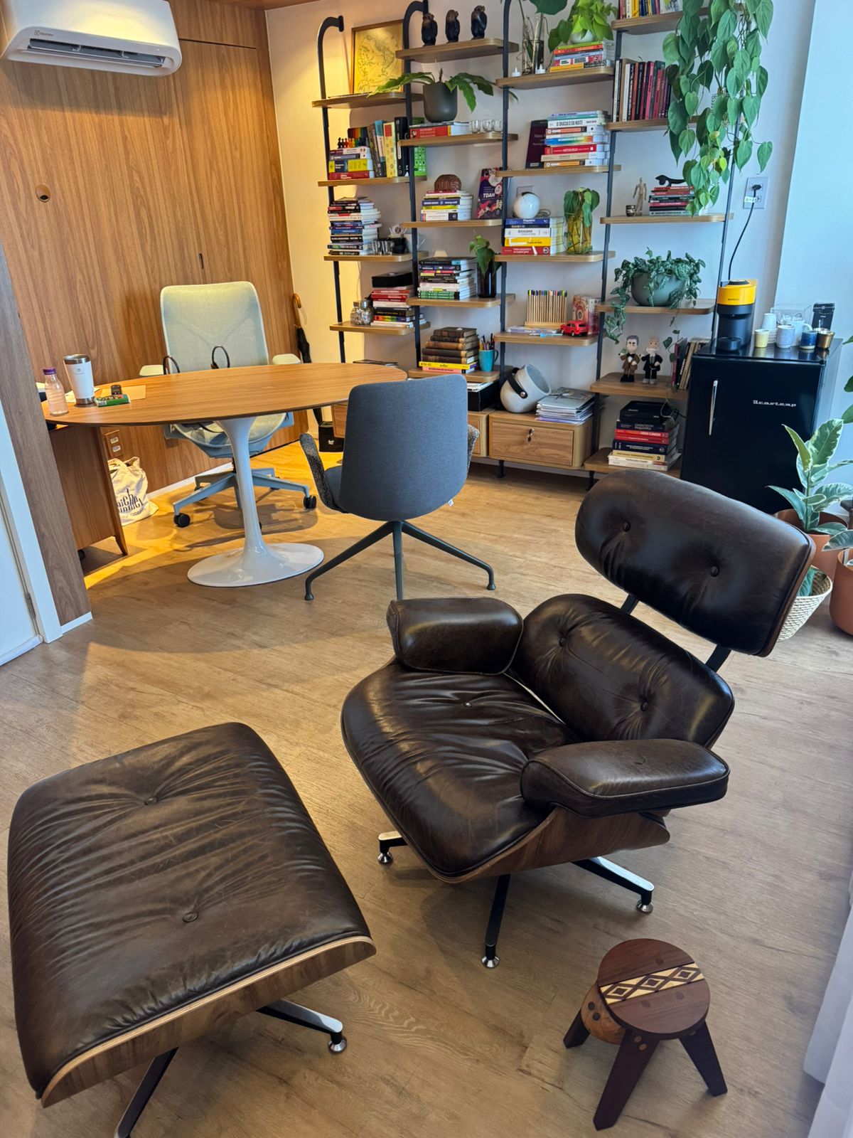 Poltrona Eames de couro com estantes e mesa oval ao fundo