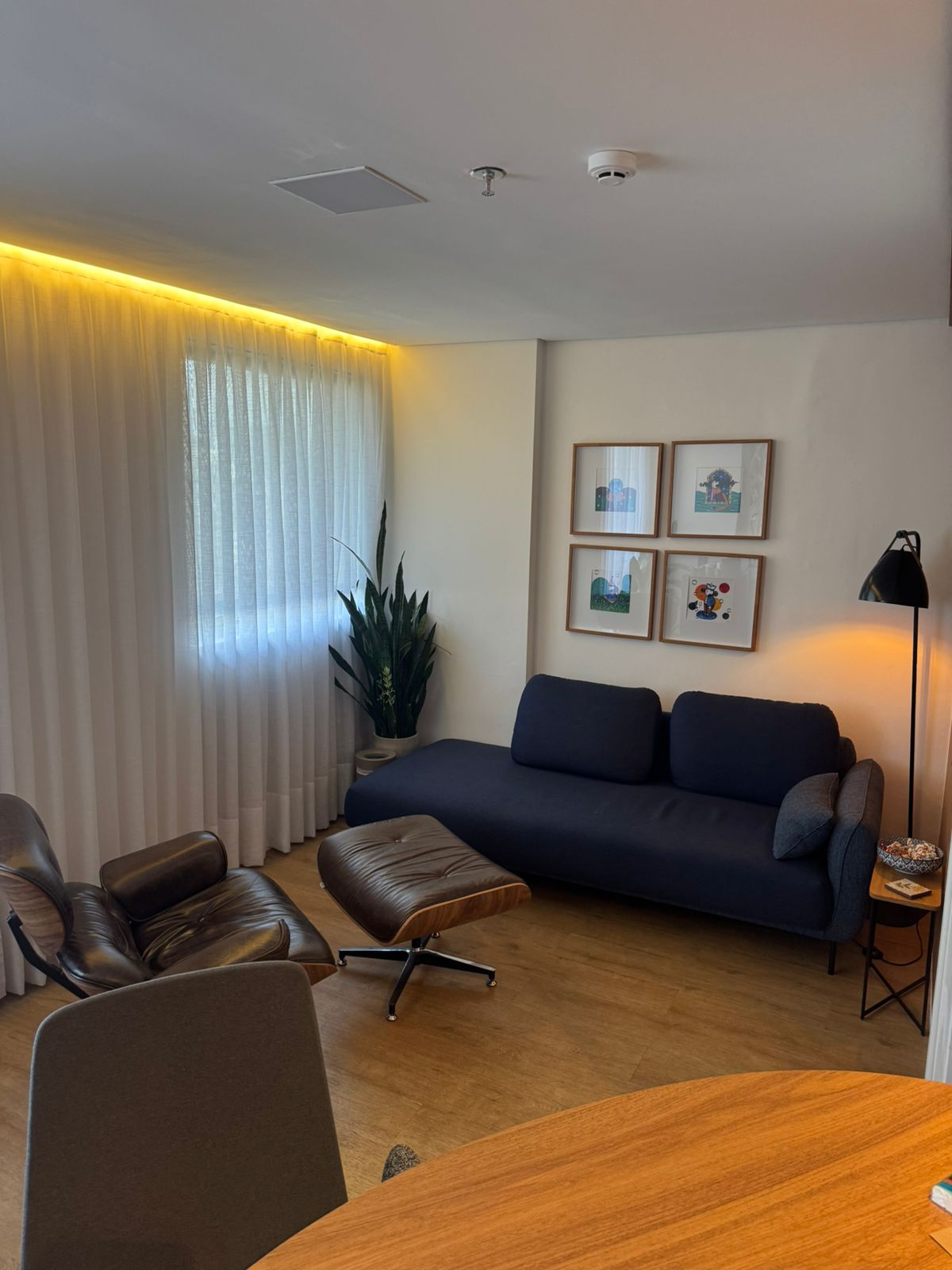 Sala de terapia com sofá azul-marinho, poltrona Eames e cortinas brancas